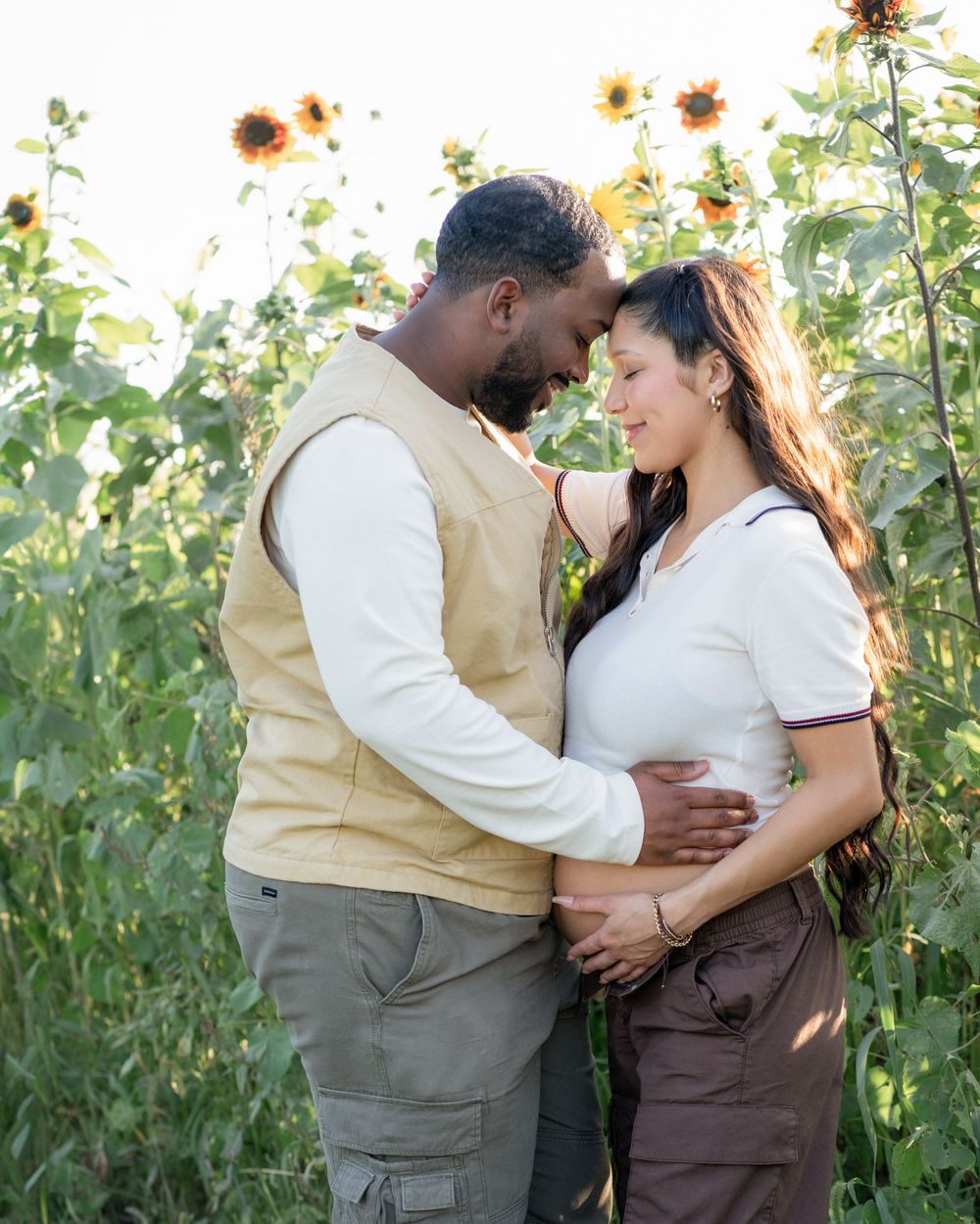 A romantic couple shares an intimate moment among tall sunflowers in a garden setting during golden hour.