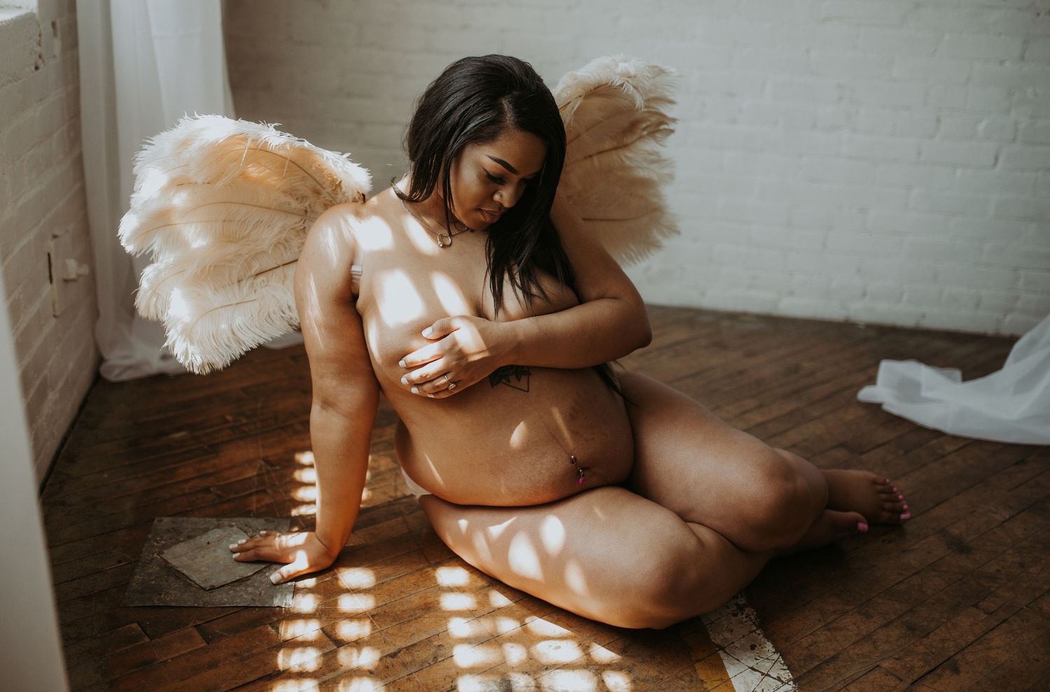 Artistic maternity photo with ethereal white curtains and natural window light illuminating an expectant mother in intimate pose.