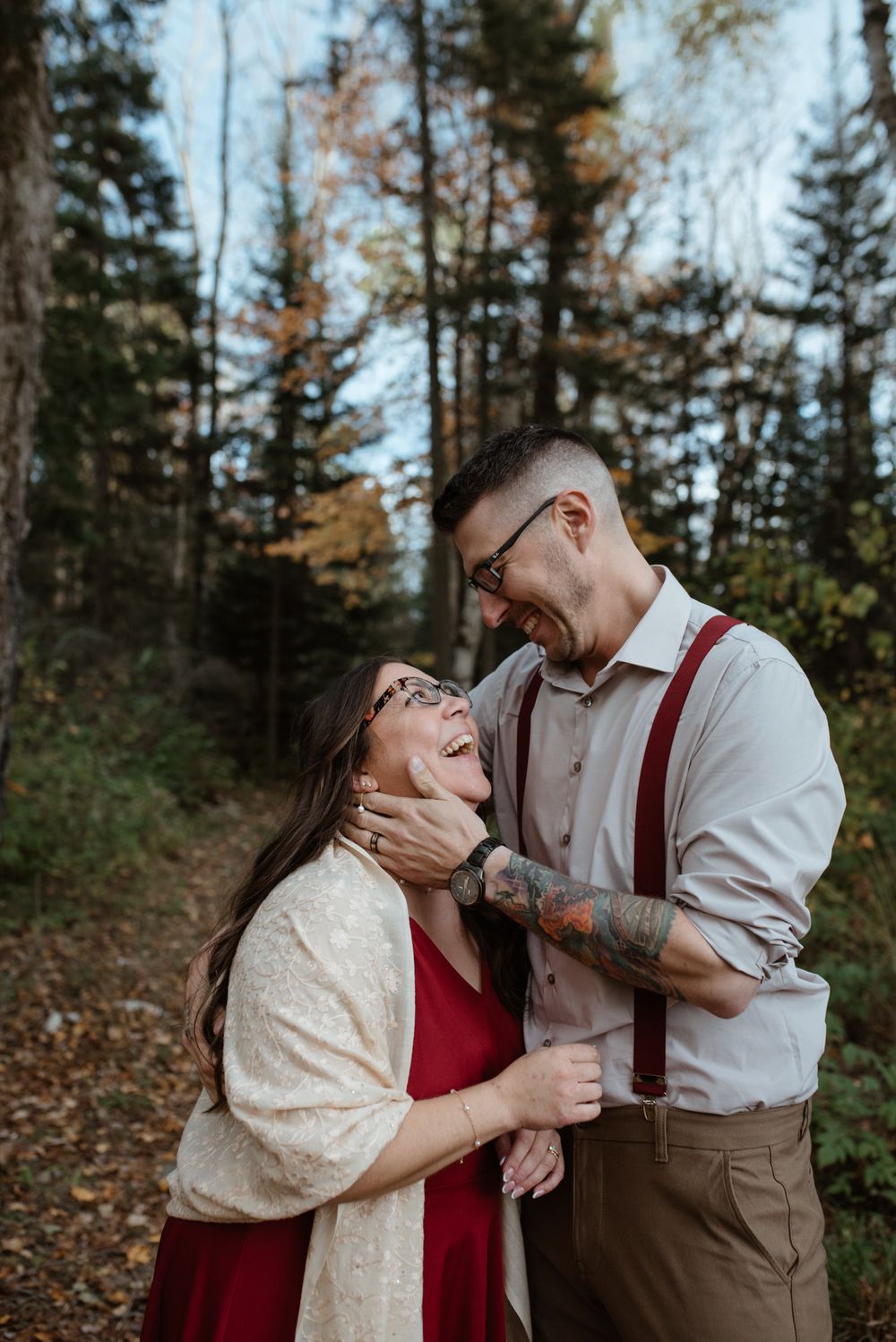 A couple shares a joyful moment together in an autumn forest setting wearing coordinated formal attire.