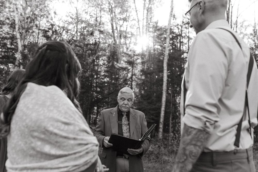Black and white photo of an intimate ceremony moment in a wooded setting.