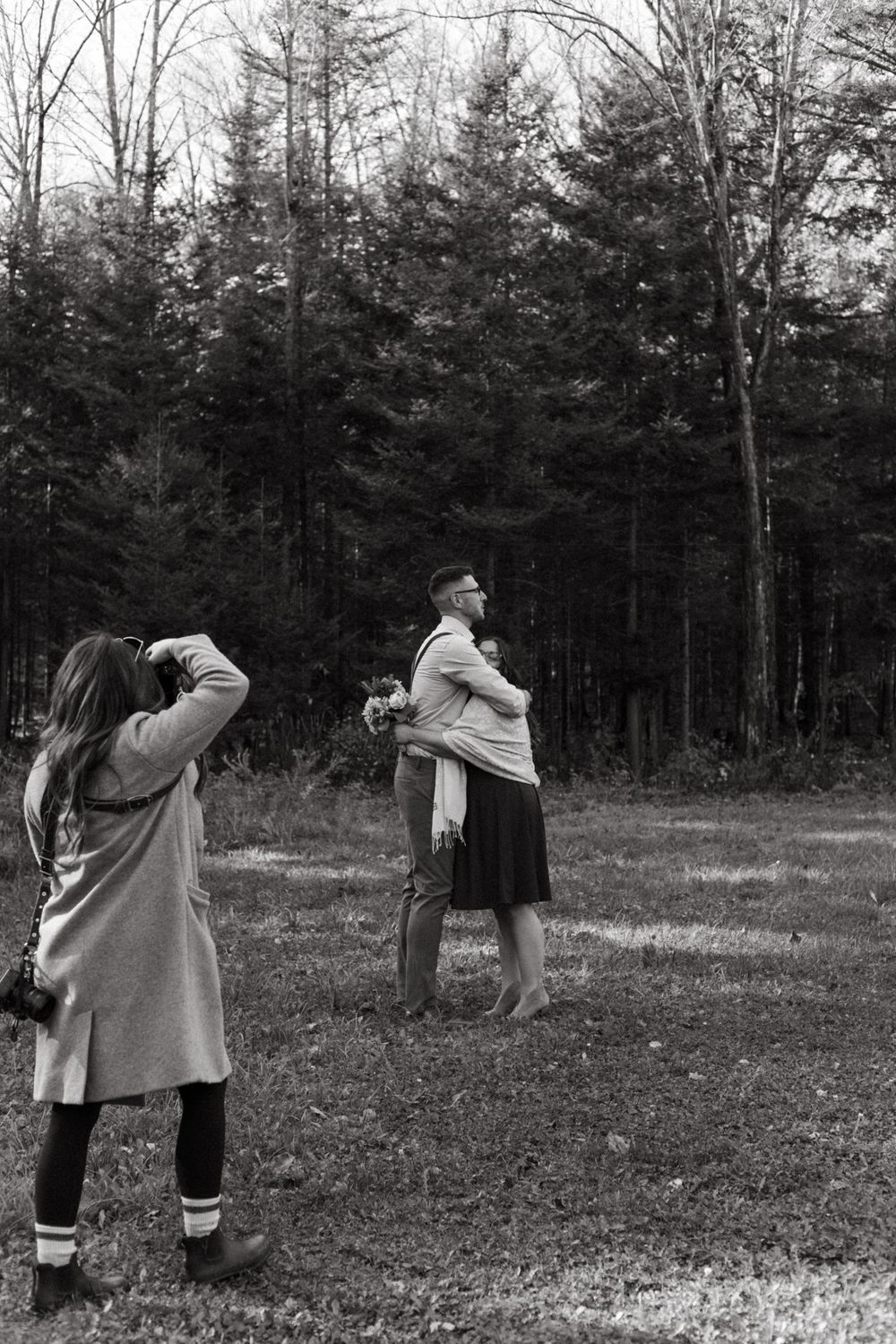 A photographer captures a moment during an outdoor fall photoshoot in a forest clearing.