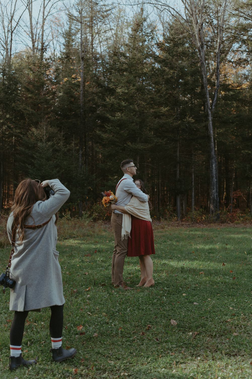 A photographer captures a couple's intimate moment in a forest clearing during autumn.