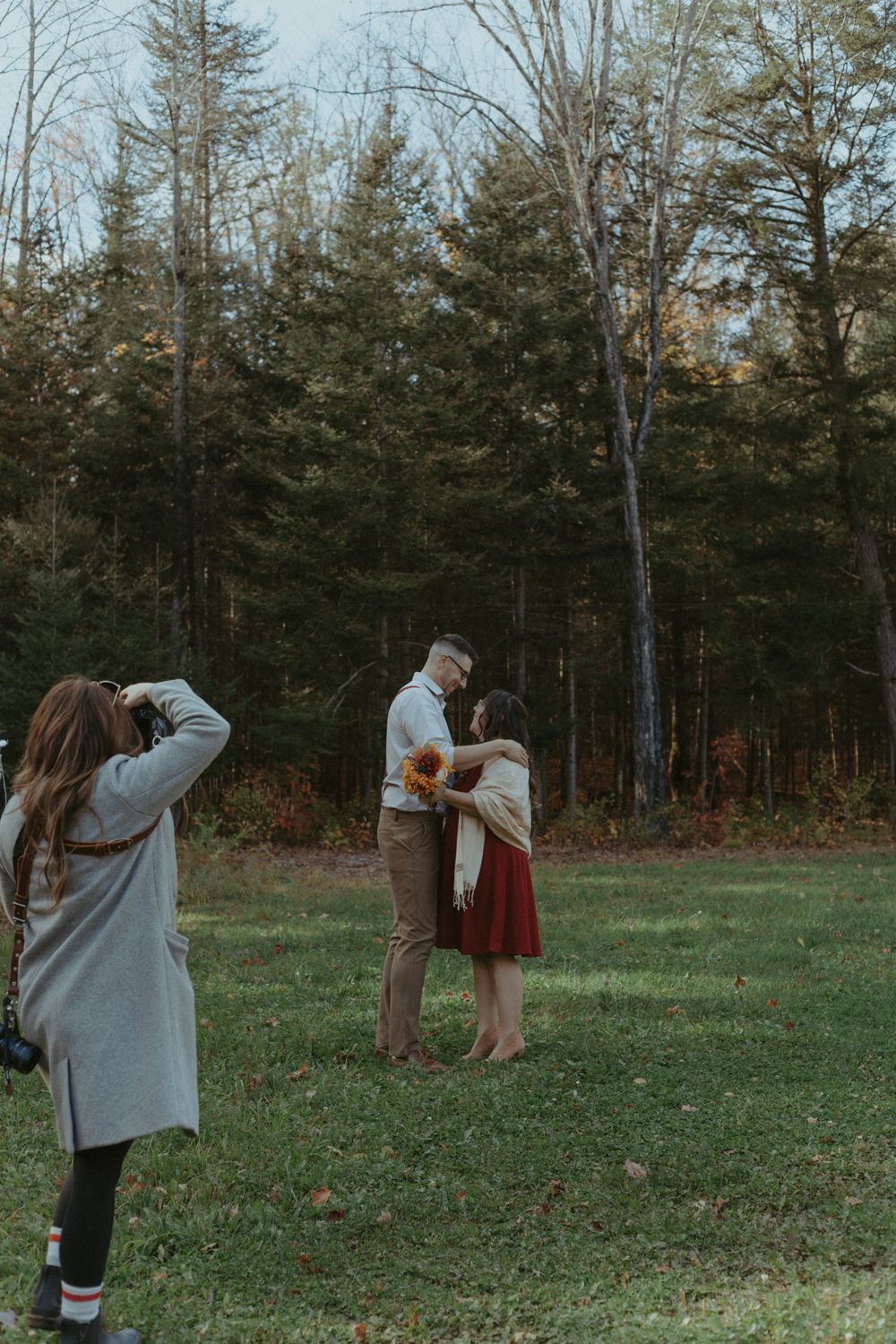 A photographer documents a romantic scene in a wooded area during fall season.