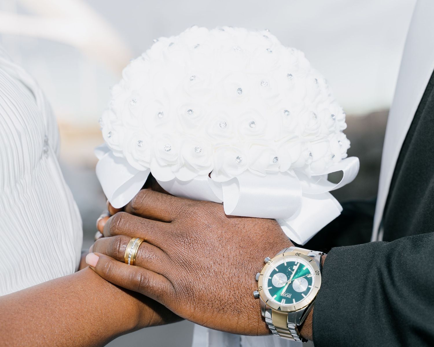 Close-up of couple holding white pearl bridal bouquet with wedding rings and luxury watch.