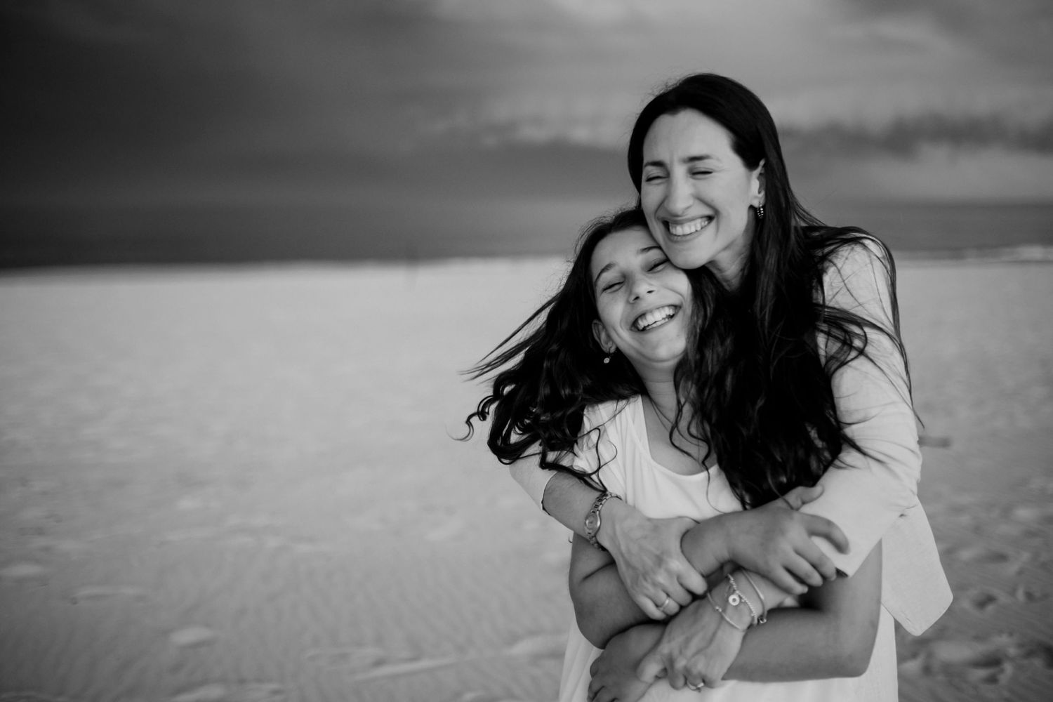 Black and white portrait of two people embracing joyfully on a beach.