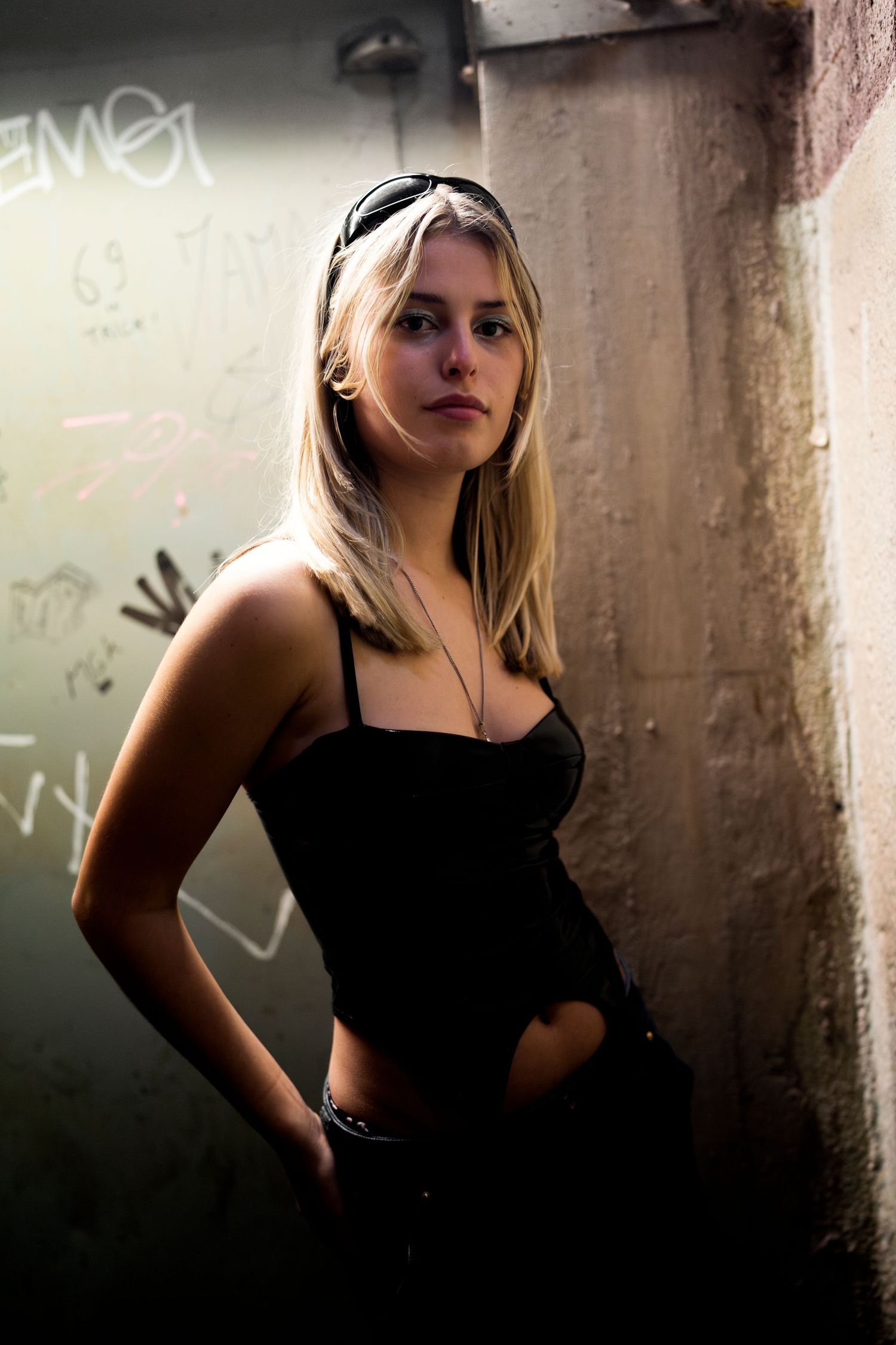 Artistic fashion portrait in a moody urban setting with grungy concrete walls and dramatic shadows.