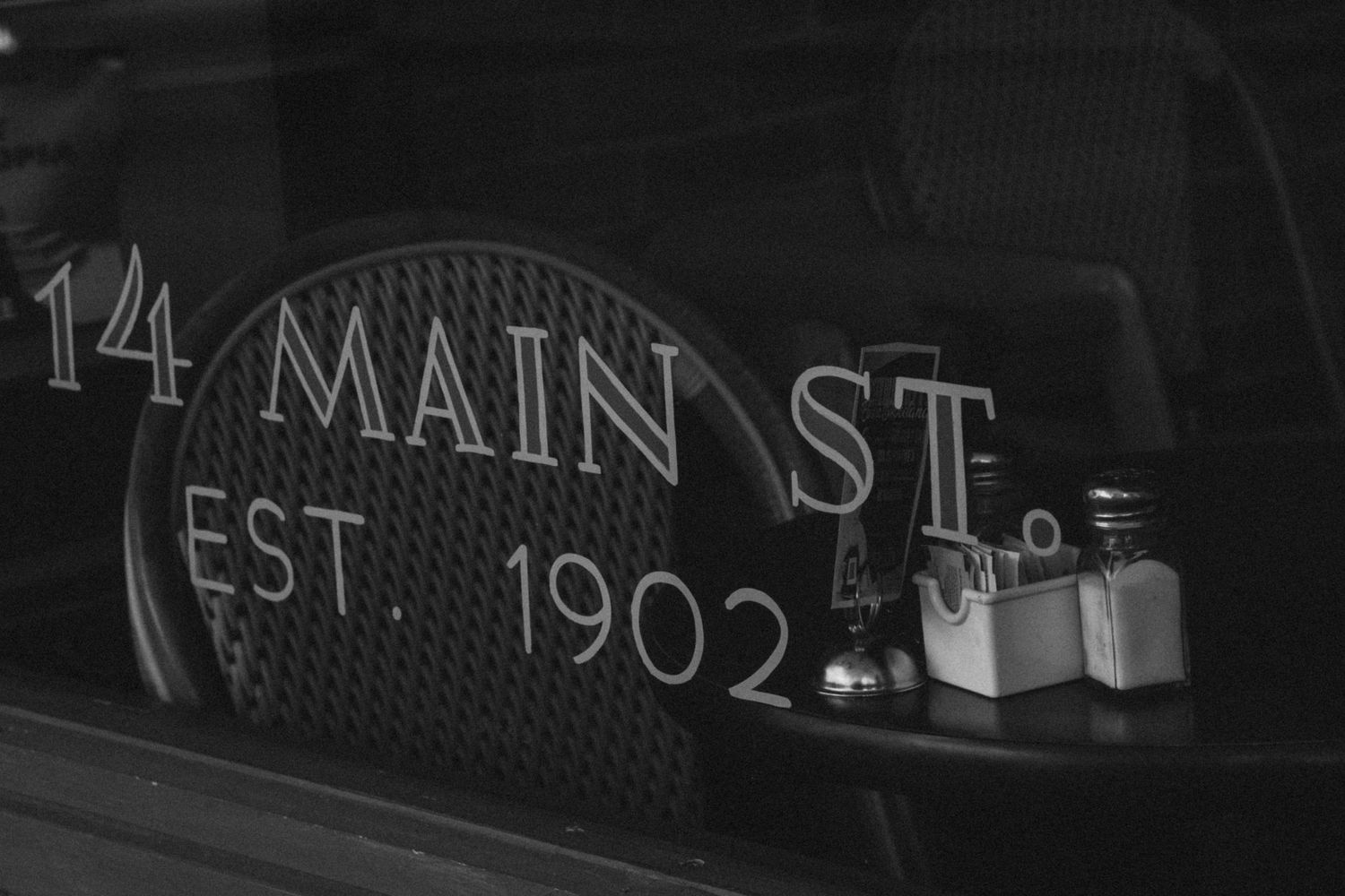 Vintage storefront window displaying '14 Main St Est 1902' text in black and white.