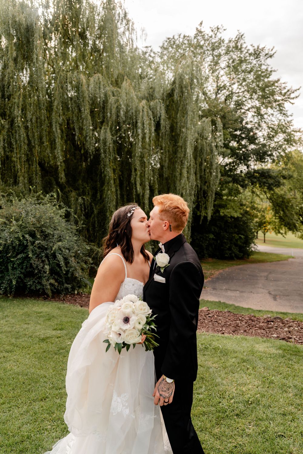 A couple sharing a romantic kiss in front of a weeping willow tree.