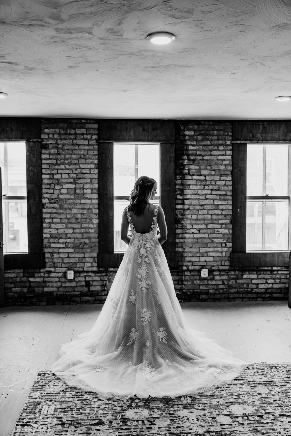 Black and white photo of bride in lace gown silhouetted against industrial windows.