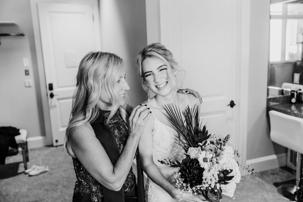 Black and white candid moment of friends sharing laughter while holding wedding bouquet.