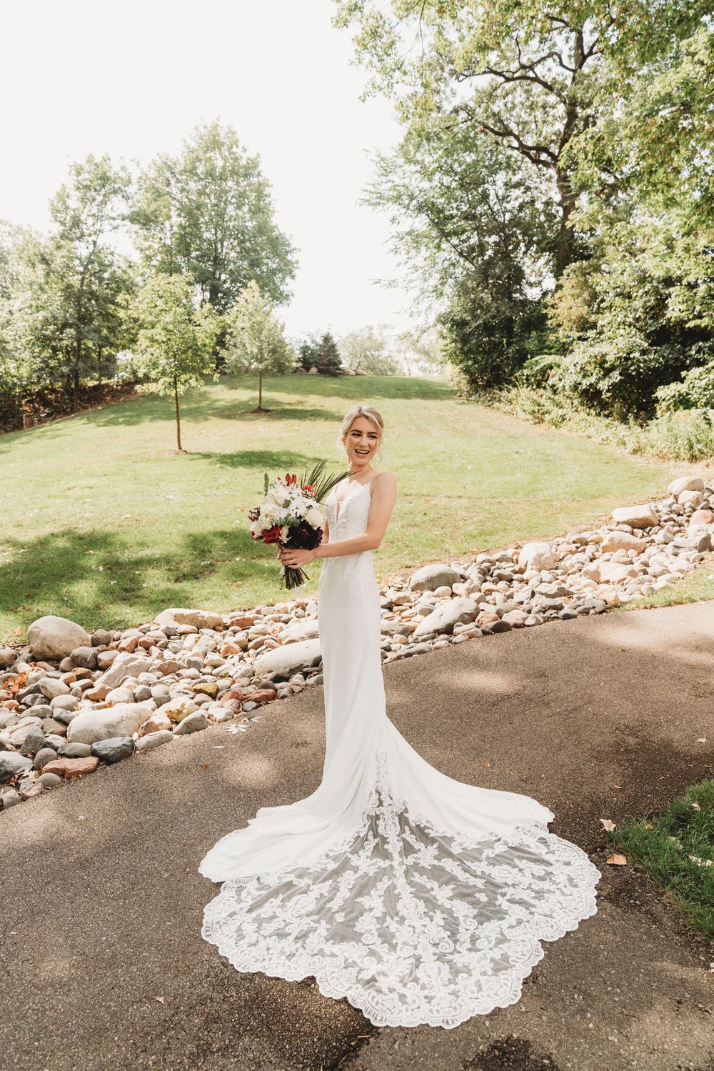 Full-length shot of bride in flowing lace wedding gown with dramatic train on outdoor path.