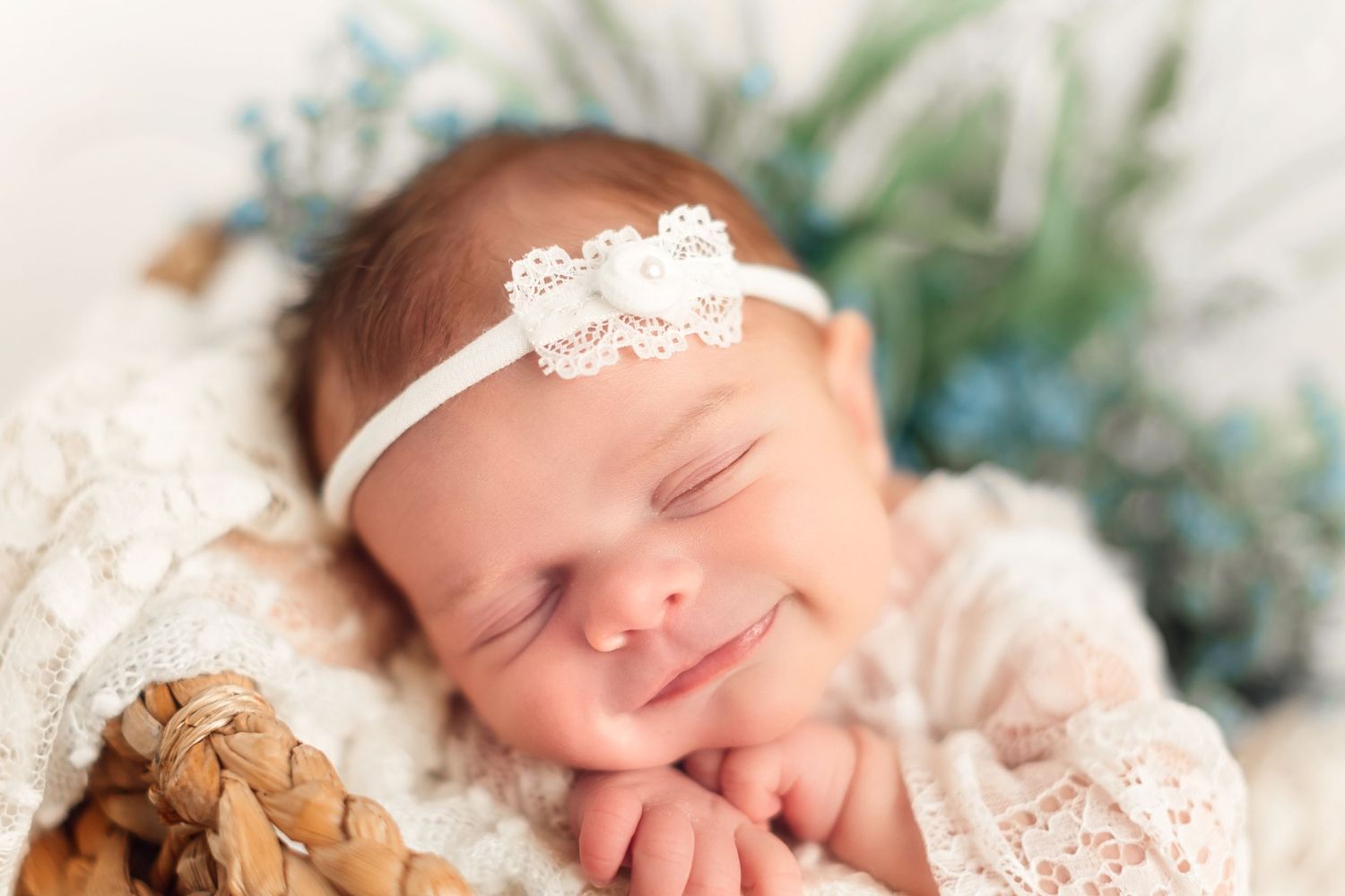 Sleeping newborn baby wearing a lace headband on soft floral backdrop.