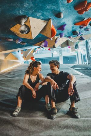 Two climbers in athletic wear sit together and chat at an indoor climbing gym with colorful climbing holds overhead at Bouldering Project
