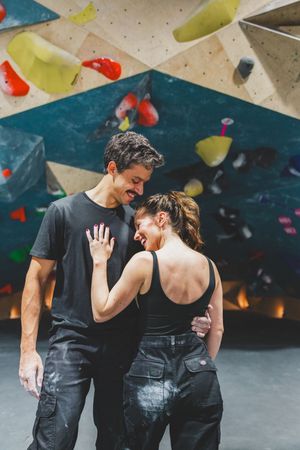 Two climbers share a happy moment together while taking a break at an indoor rock climbing gym with colorful walls.