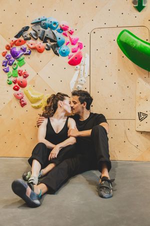 Climbers in black clothing resting at the base of an indoor climbing wall decorated with colorful holds.