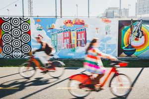 Two cyclists ride past colorful street art murals on a wall featuring geometric patterns and whimsical designs in Washington DC
