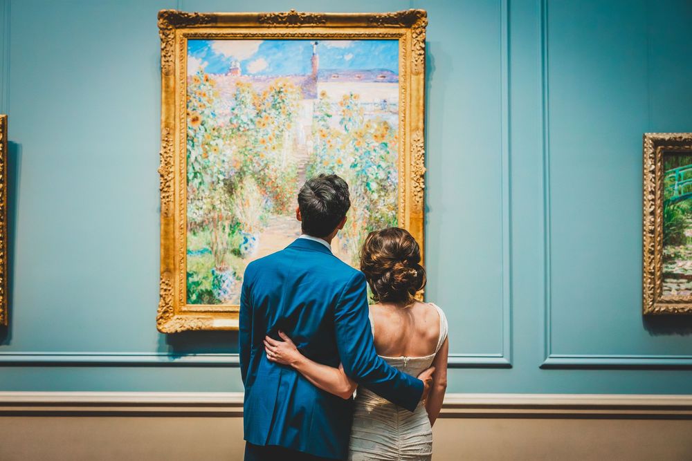 Couple in blue attire admires colorful impressionist paintings displayed in gallery with turquoise walls at National Gallery Of Art in DC
