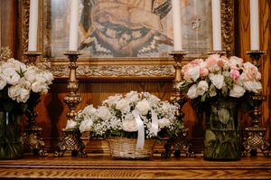Elegant floral arrangements with white and pink roses displayed on wooden mantle with ornate artwork backdrop.