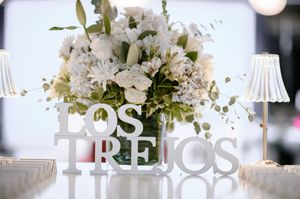 Elegant white floral centerpiece arrangement with 'Los Tres' text display at an upscale event setting.