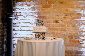 Three wedding cake design mockups against rustic brick wall showing white buttercream tiers with black and gold accents.
