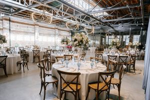 A modern industrial wedding reception venue with cross-back chairs, round tables, and white floral centerpieces.