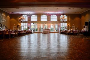 Large empty ballroom with wooden dance floor, arched windows, and elegant decor set up for a formal event.
