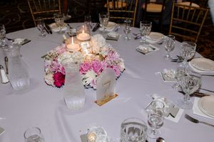 Elegant wedding reception table setting with pink floral centerpiece, glowing candles, and crystal glassware on white tablecloth.