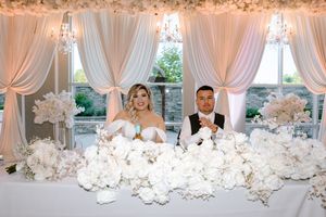 Luxurious wedding table decorated with white drapery, crystal chandeliers, and abundant white floral arrangements.