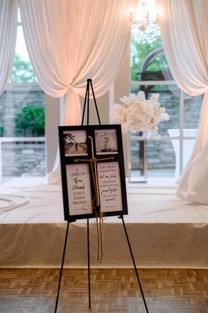 Row of decorative welcome signs displayed on black easels in front of white draped backdrop at wedding venue entrance.
