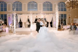 Dancing couple surrounded by white fog on a grand ballroom floor with large windows and elegant lighting.