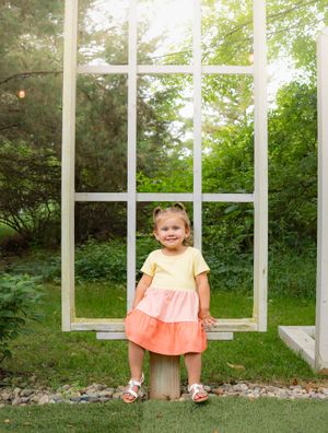 A sweet moment captured in front of a large window frame with lush greenery in the background.