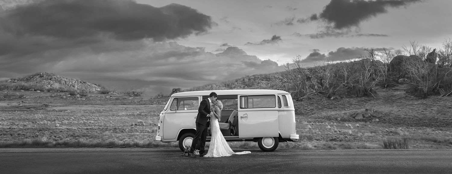 Bride and Groom sharing a moment and a kiss holding a glass of Champagne standing in font of the Kombi wedding van with