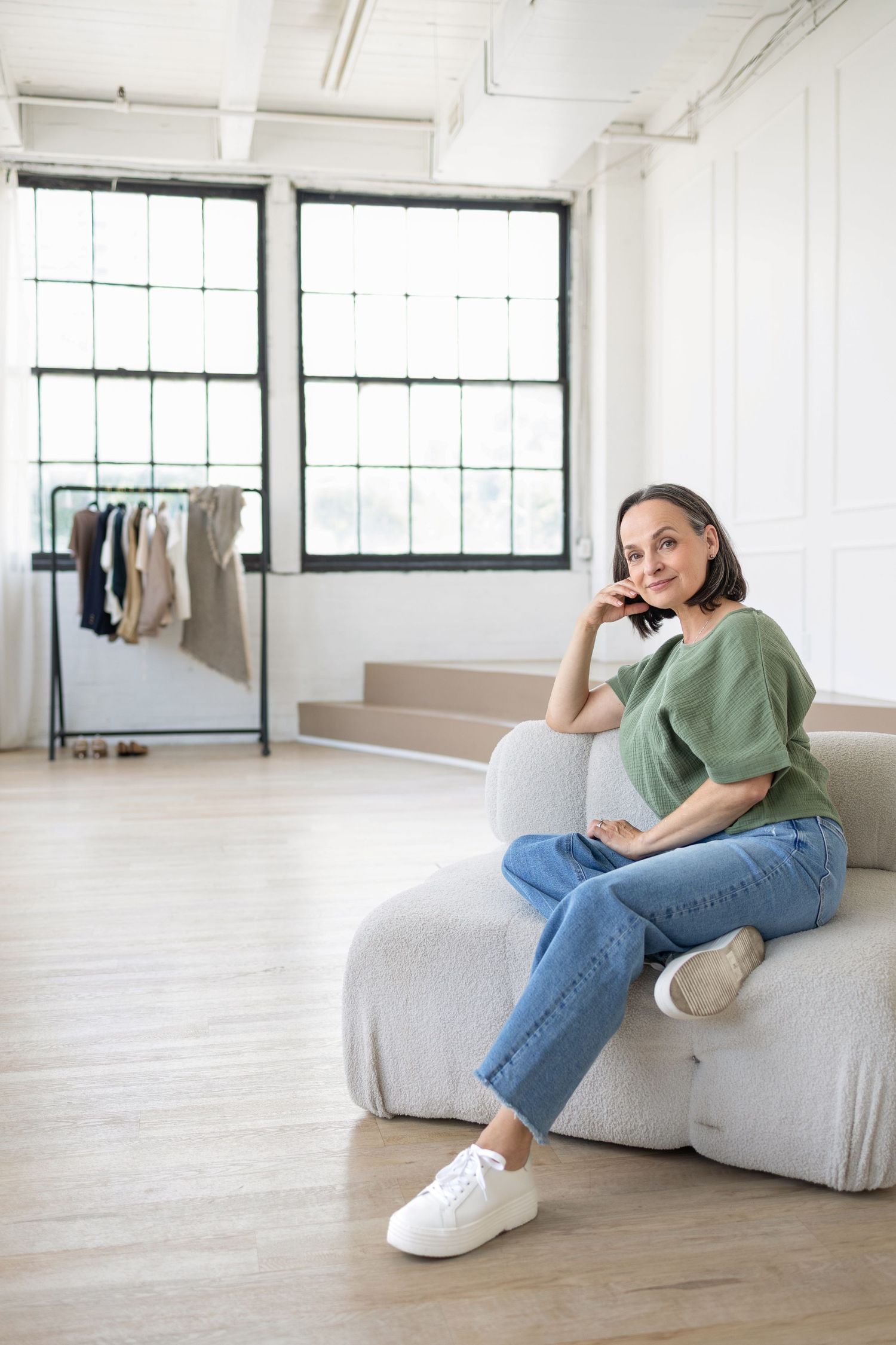 Lifestyle branding portrait of a wardrobe consultant seated casually in a bright studio, relaxed and approachable.