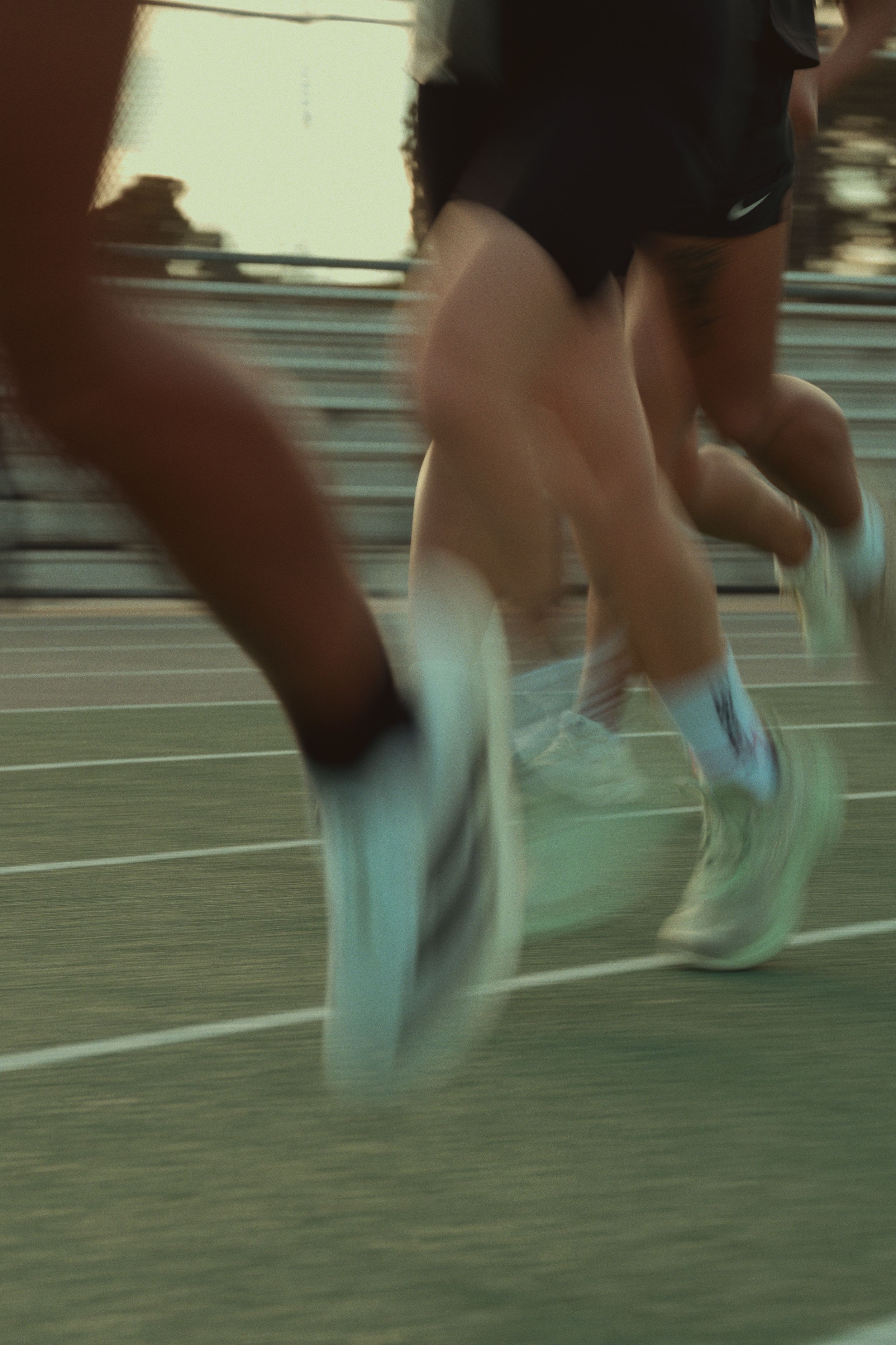 Motion-blurred legs and feet of runners sprinting on a track wearing light-colored athletic shoes.