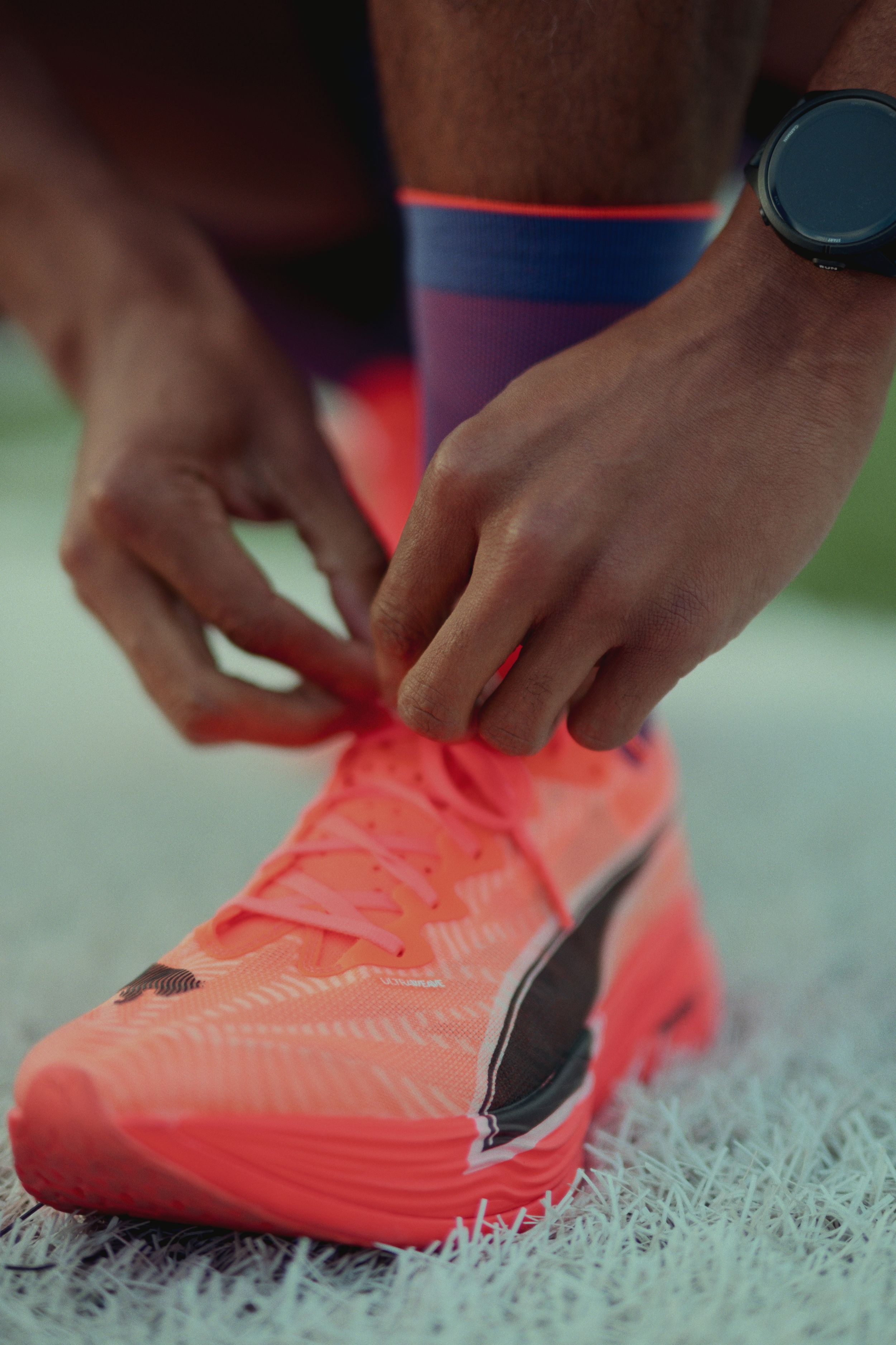 Close-up of hands tying bright coral Puma running shoes on a textured gray surface.
