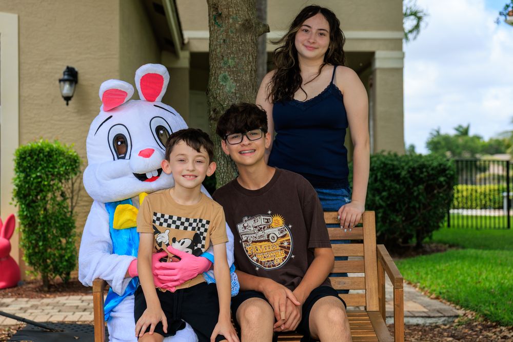 Two kids pose with Easter Bunny character and a teenage girl outside a house during an Easter celebration.
