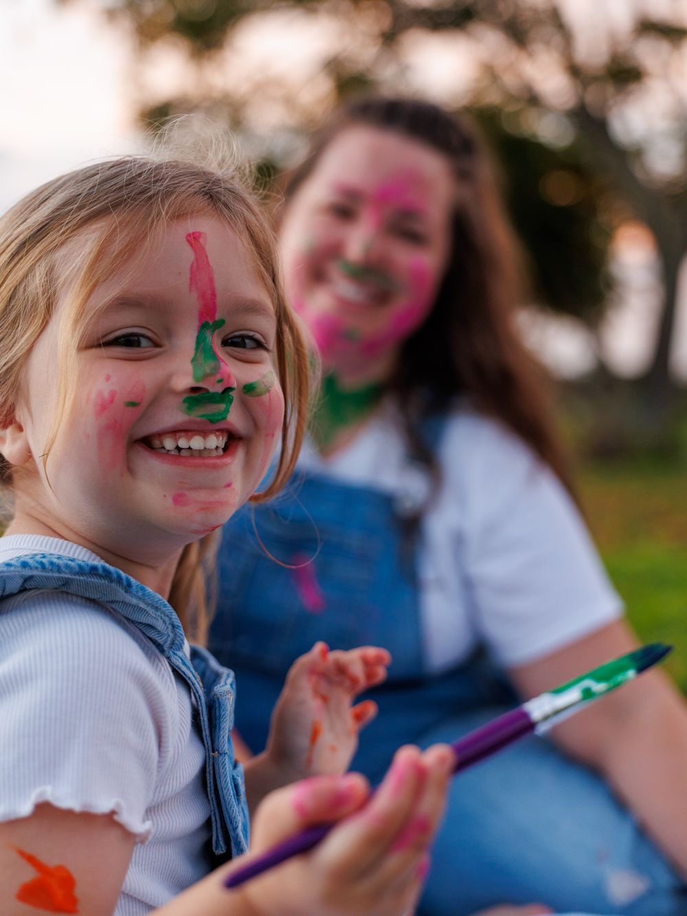 Children with colorful face paint smile and play with markers during an outdoor activity.