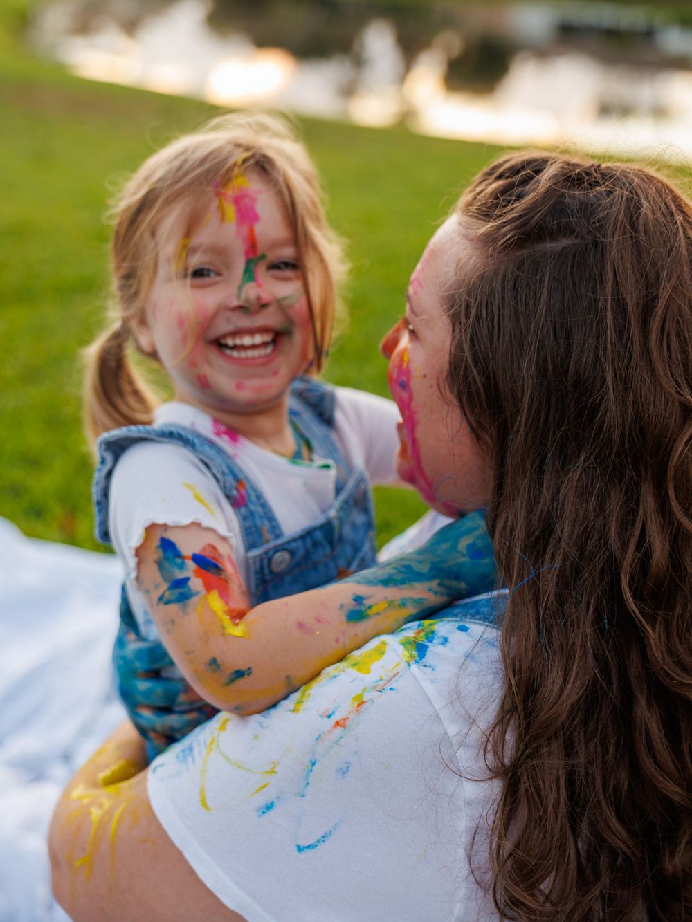 Two children playing with colorful paint on their faces and clothes while laughing together outdoors.
