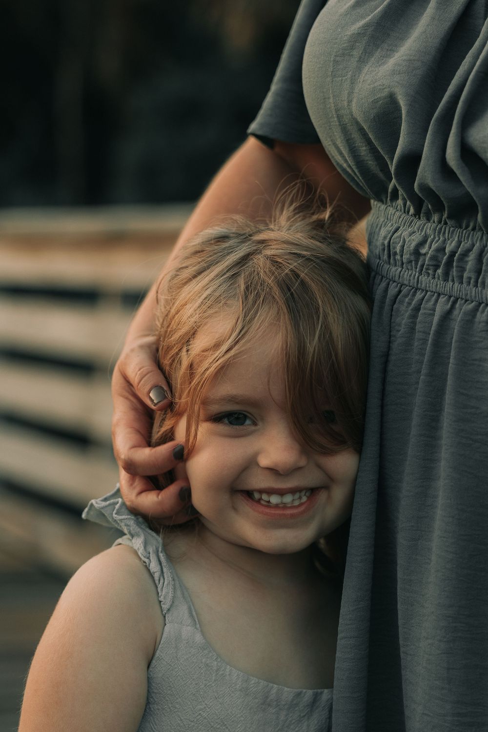 Child in a gray dress playing peek-a-boo against a dark background.