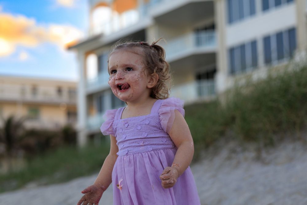 Playful moment in purple dress against coastal sunset backdrop.