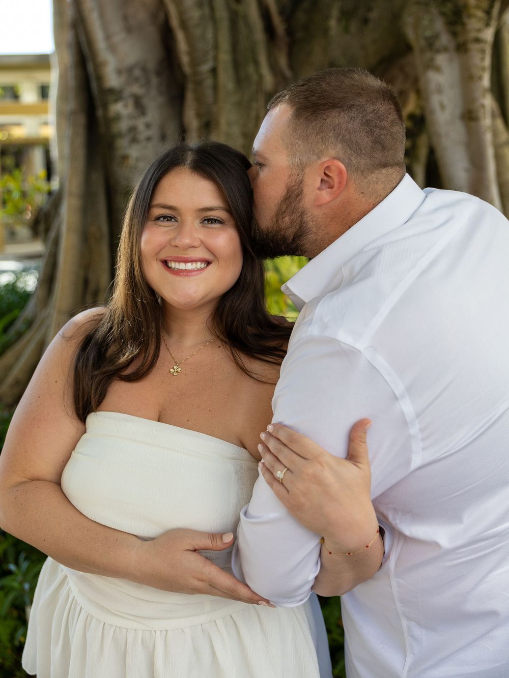 Couple embracing outdoors during a romantic photoshoot near trees.