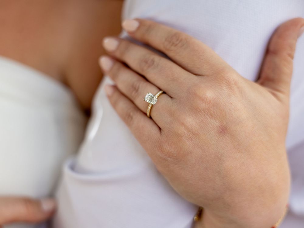 Close-up of hands displaying an engagement ring against white fabric.