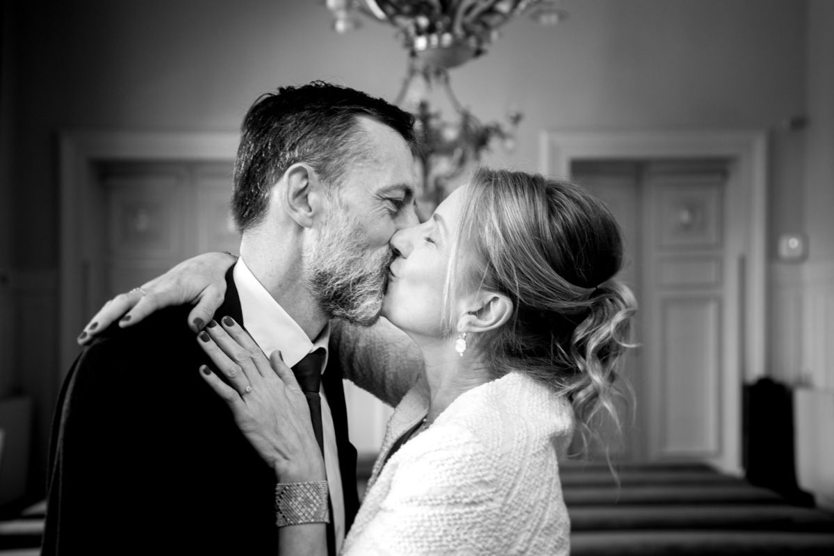A romantic black and white wedding photo shows a couple sharing an intimate kiss under a chandelier.