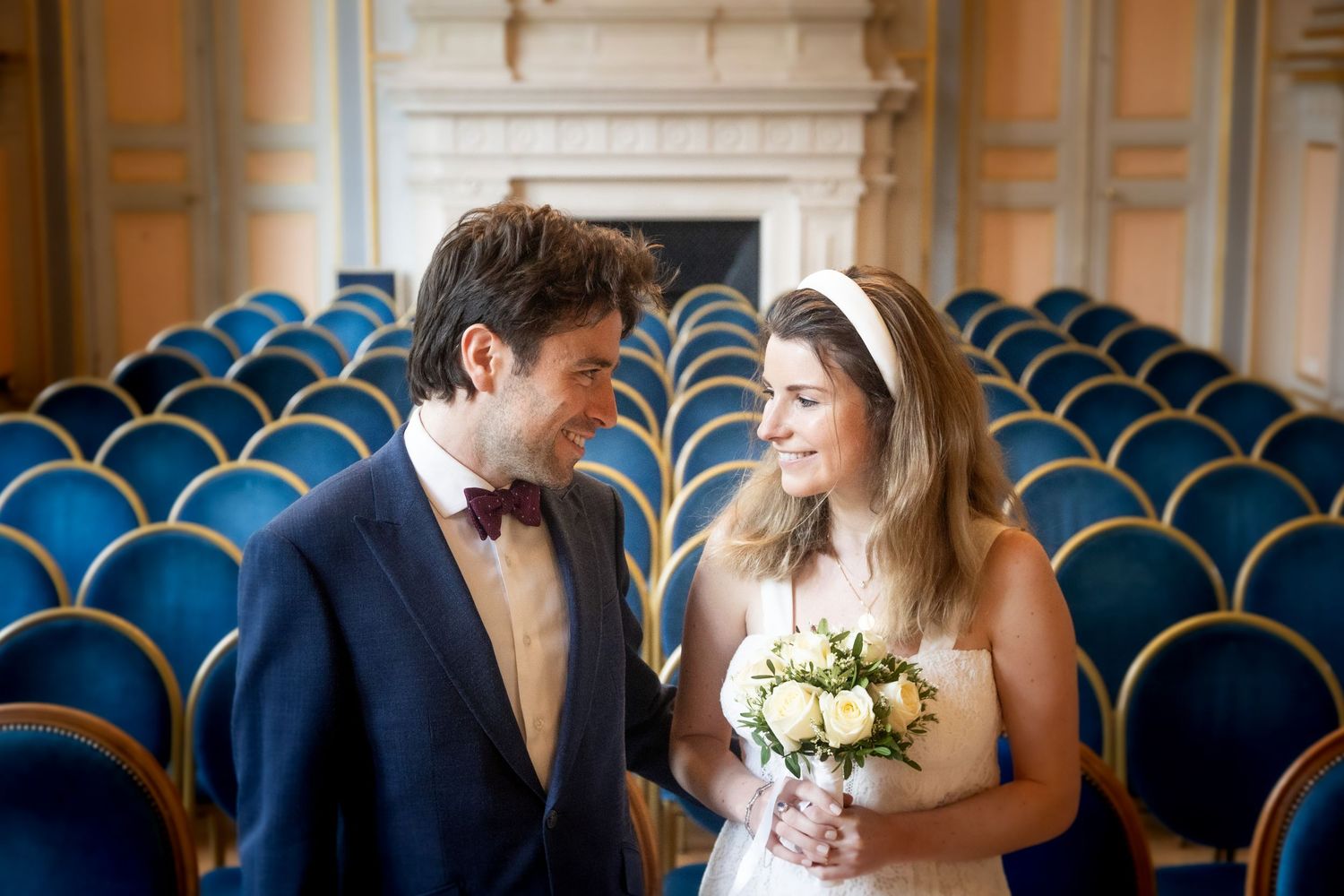 A happy couple in wedding attire share a joyful moment in an empty theater with blue velvet seats.