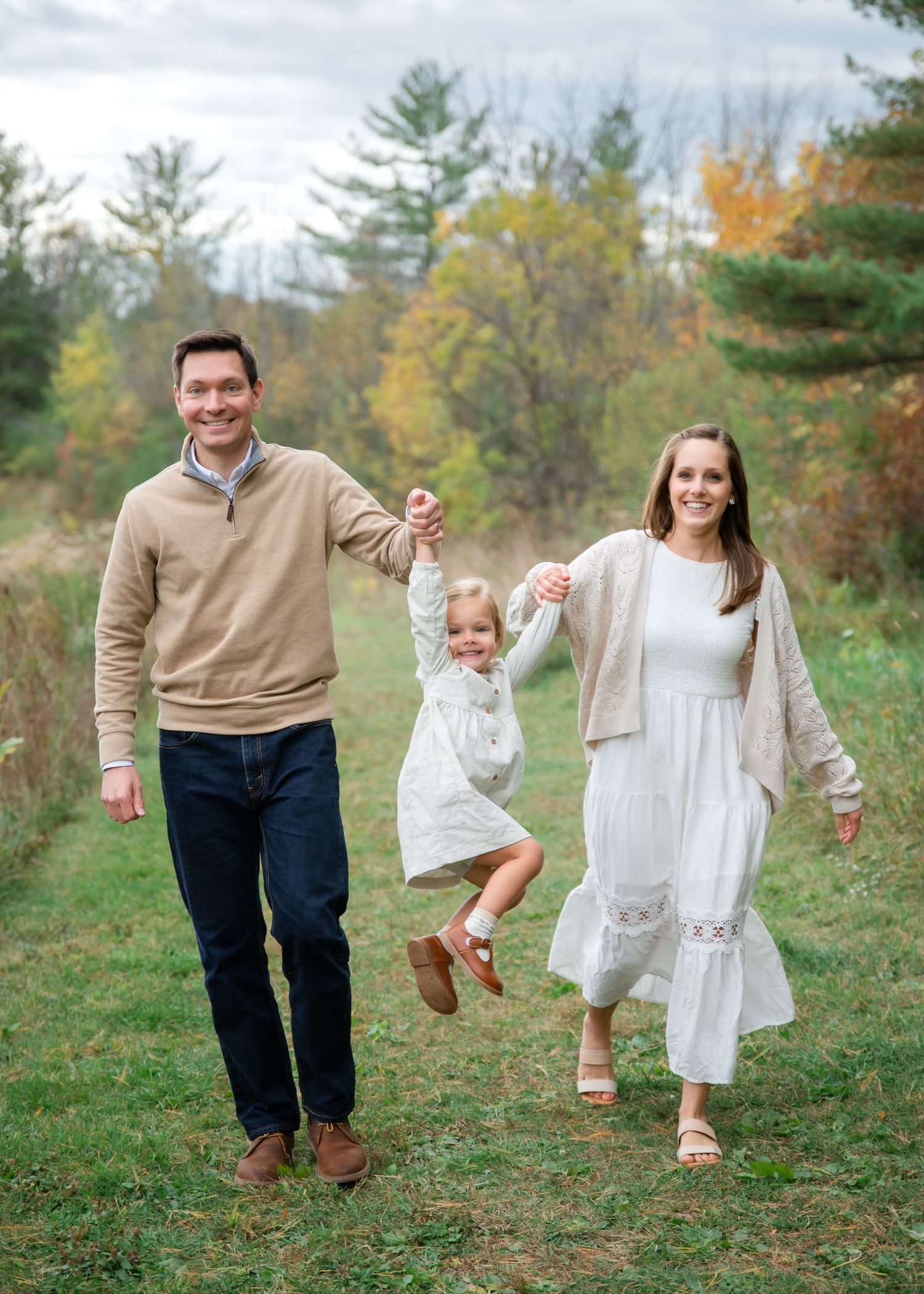 A family holding hands and playing together in an autumn forest clearing with colorful fall foliage in the background.