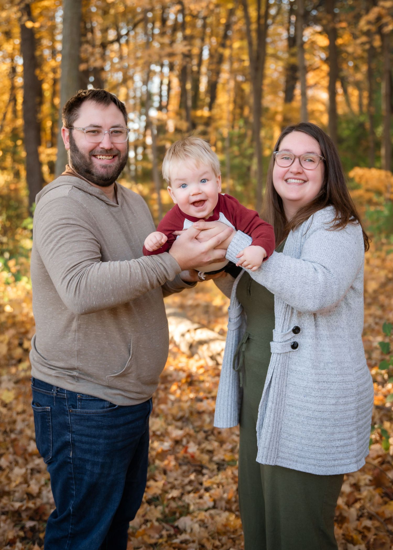 A family poses together in a beautiful autumn forest setting with vibrant orange and yellow fall foliage in the background.