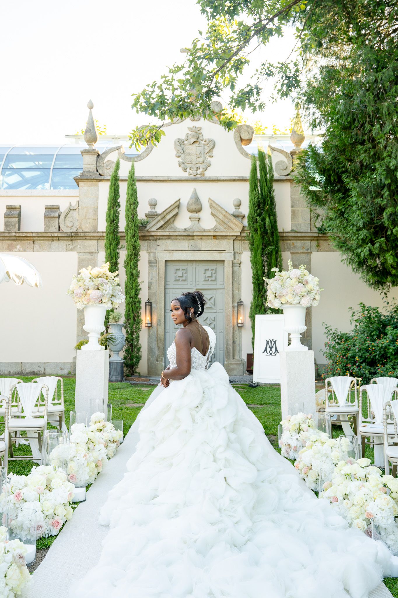 A stunning white wedding dress displayed in an elegant garden setting with classical architecture.