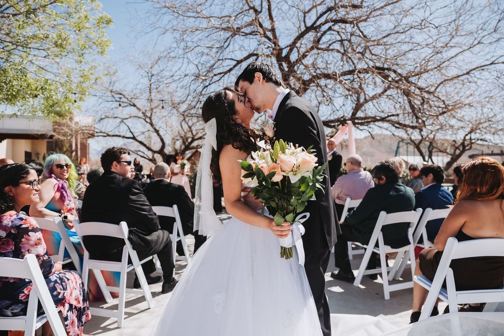 Wedding ceremony guests seated at white chairs during an outdoor celebration with cherry blossoms in bloom.