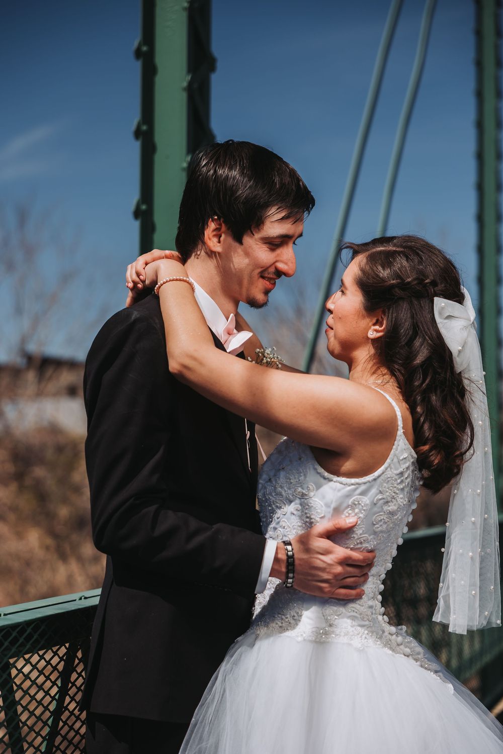 A joyful wedding couple embraces on a green metal bridge during their outdoor photo session.