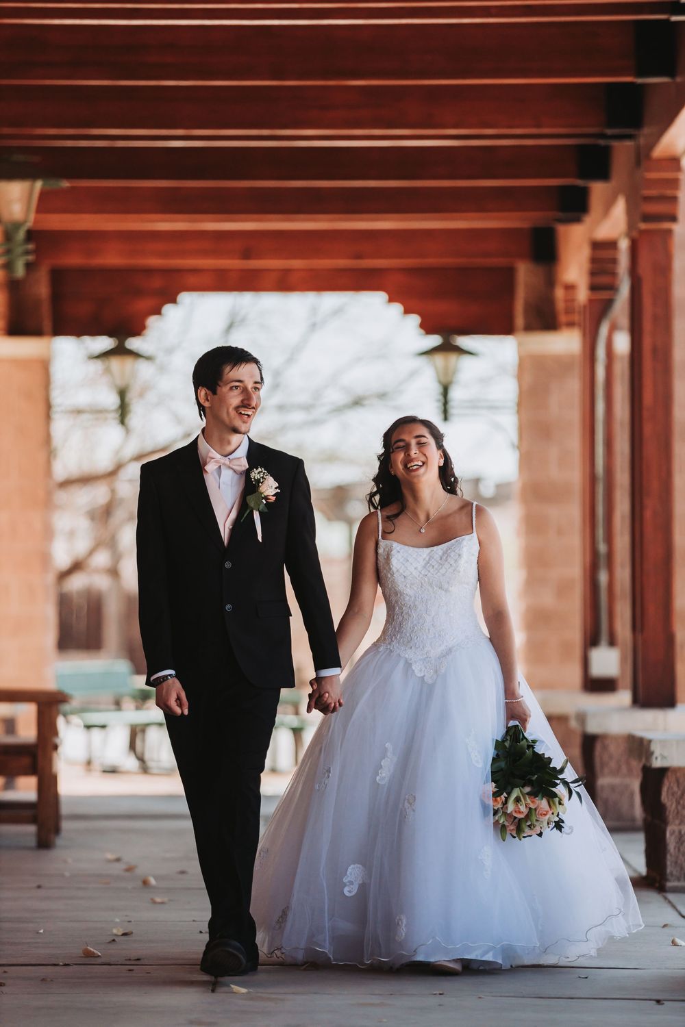 A joyful couple holding hands while walking under rustic wooden beams during their wedding ceremony celebration.